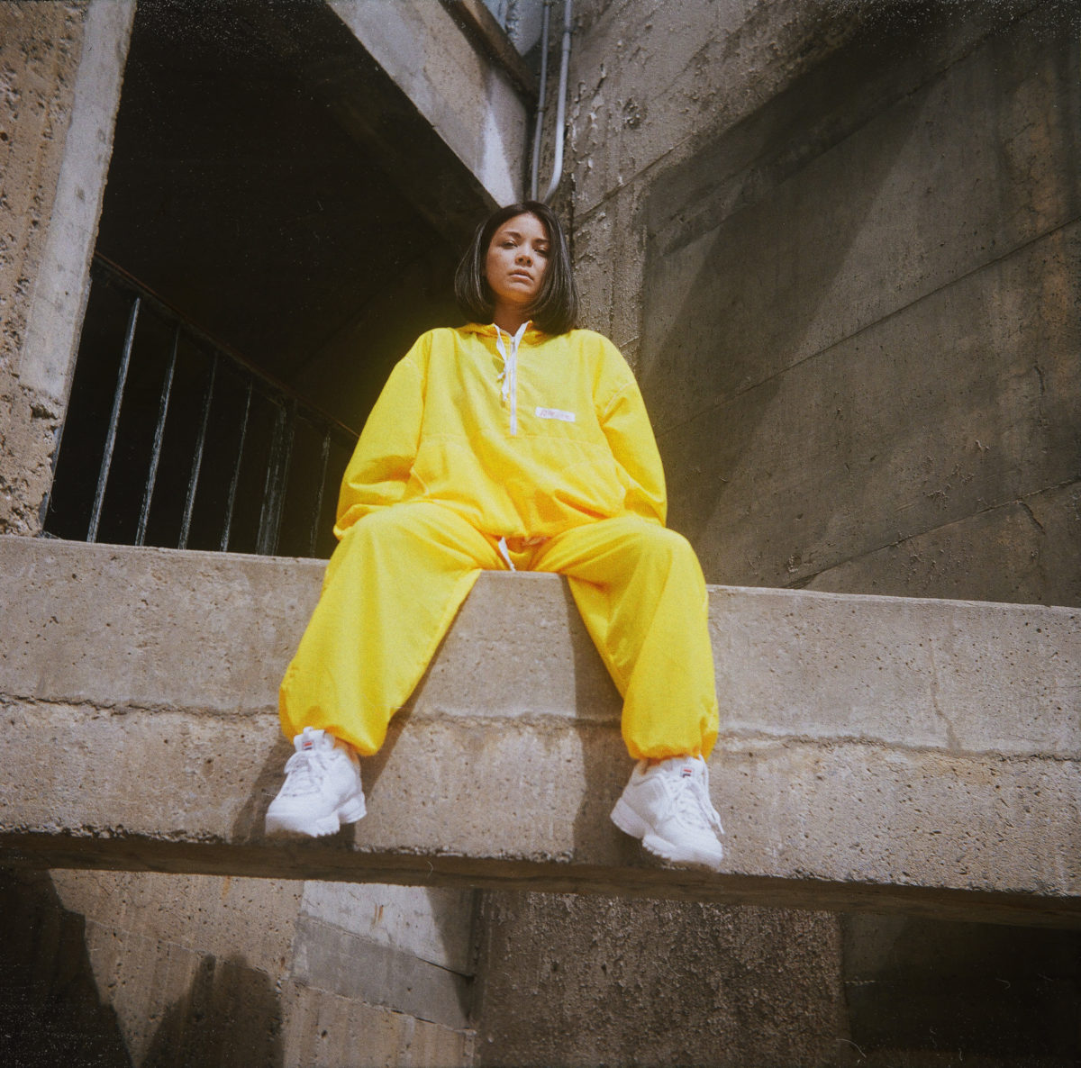 Aki, sitting on a cement ledge, wearing a bright yellow track suit